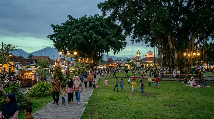 Alun-alun kota yang teduh dengan pepohonan dan warga bersantai di sore hari